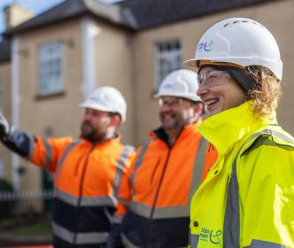 Two engineers wearing orange safety gear and another wearing a yellow high visibility jacket with a helmet
